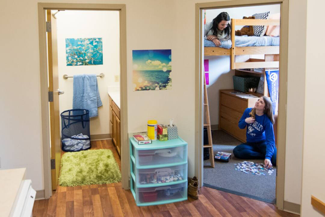 Roomates talk in a 2-bedroom apartment style unit. Featured are two bedrooms and a living area.